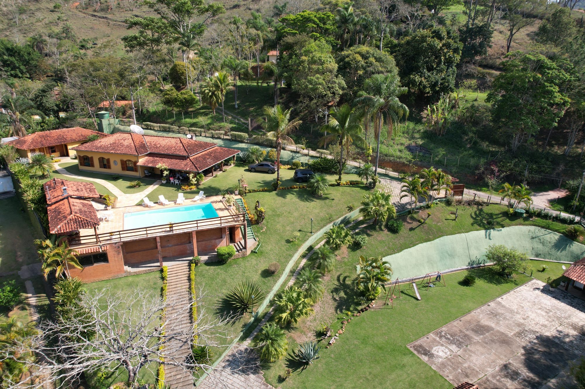 Vista aérea do jardim amplo, palmeiras e telhado colonial da casa