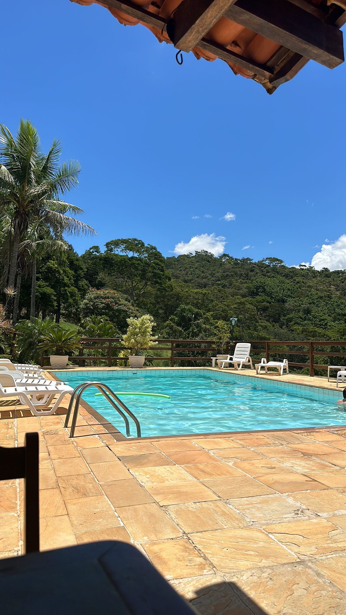 Piscina de água azul com deck de pedra e a serra ao fundo