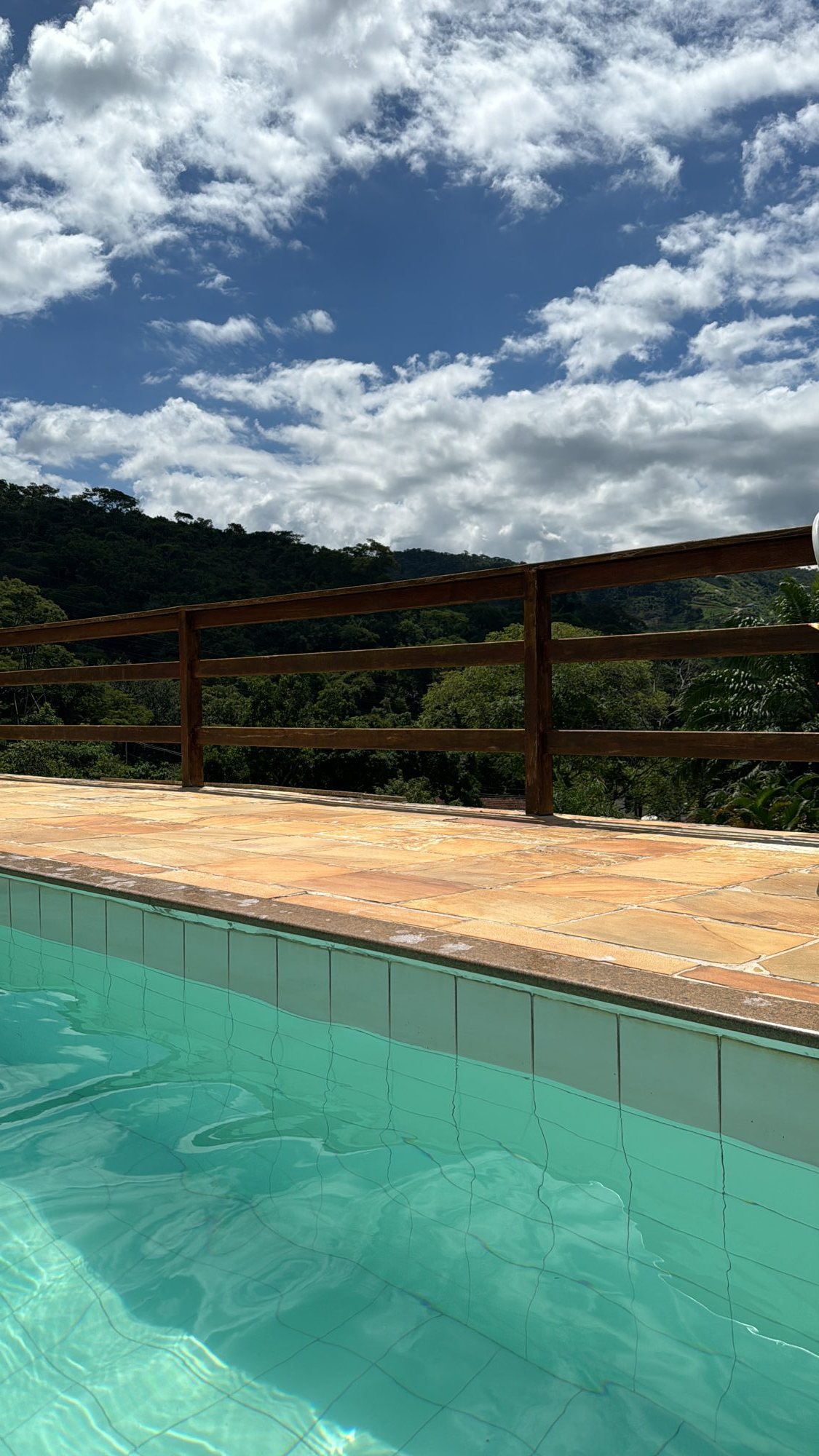 Deck de pedra ao redor da piscina com guarda-corpo de madeira